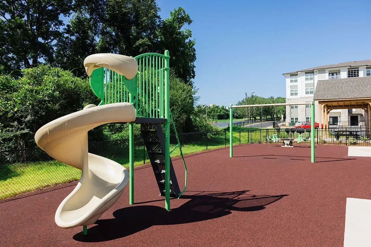 Playground with spiral slide and green climbing structure, adjacent to apartment buildings.