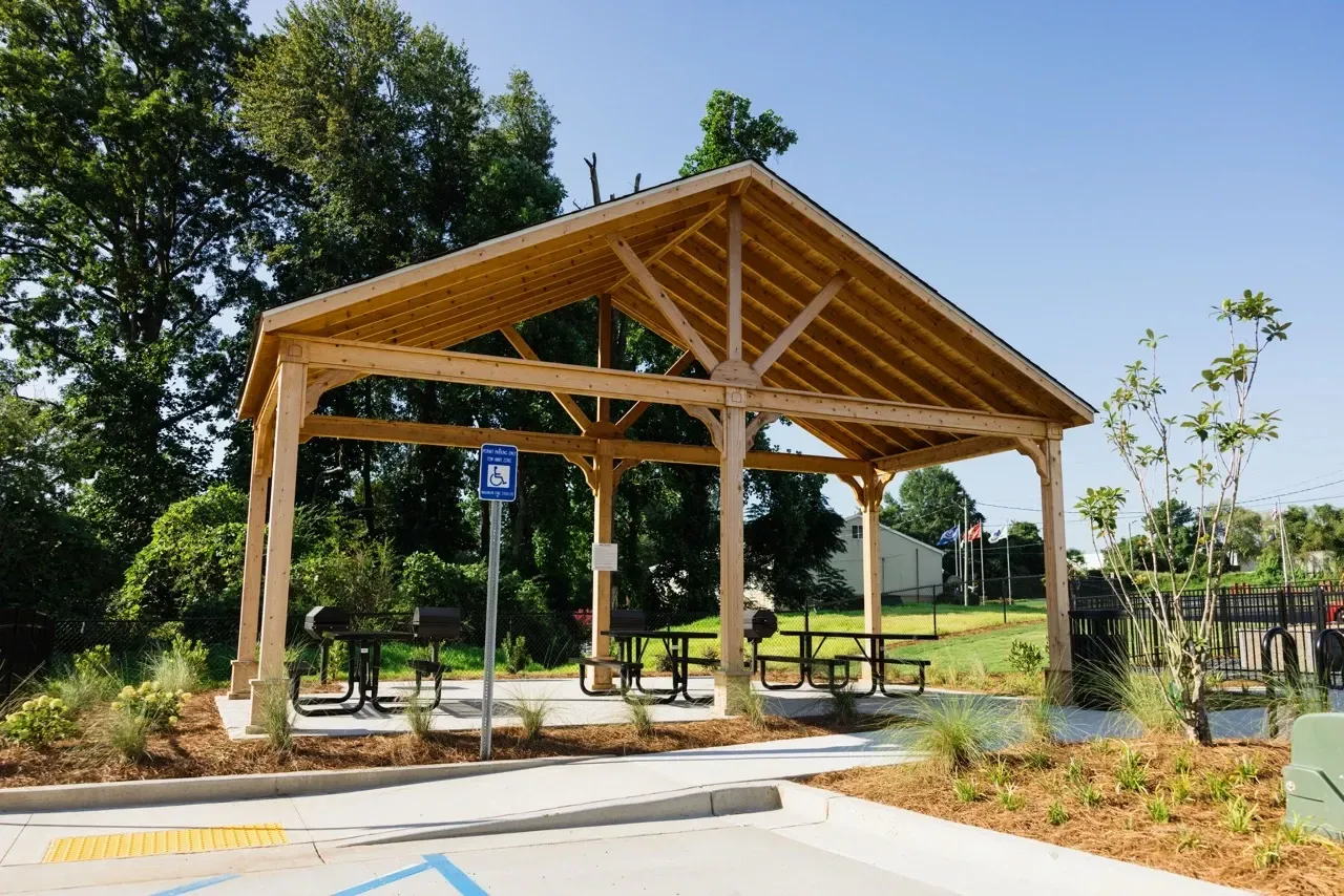 Wooden open-air pavilion with picnic tables in a landscaped outdoor common area.