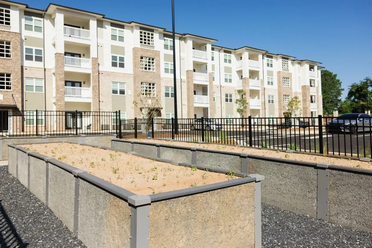 Exterior view of a multi-building apartment complex with balconies, a black metal fence, and landscaped courtyards.
