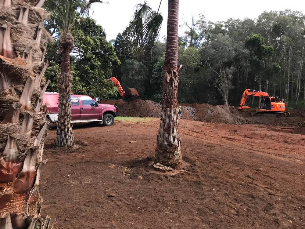 A Red Truck is Parked in a Dirt Field With a Bulldozer in the Background — Eggins Earth & Road in Byron Bay, NSW