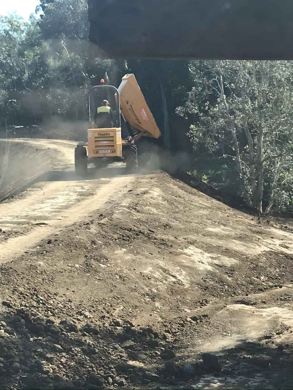 A Yellow Dump Truck is Driving Down a Dirt Road — Eggins Earth & Road in Wardell, NSW