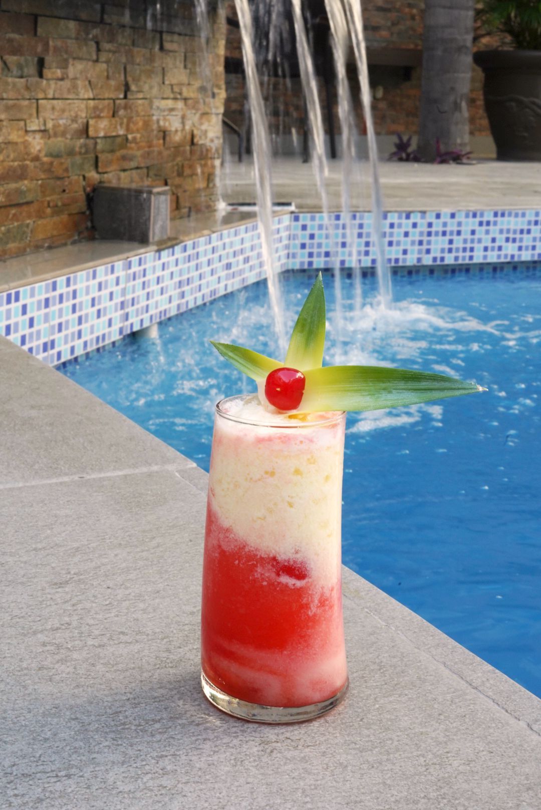 Una bebida con una cereza encima está al lado de una piscina.