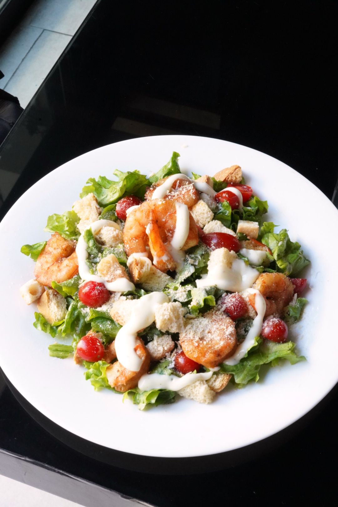 Una ensalada con camarones y tomates en un plato blanco.