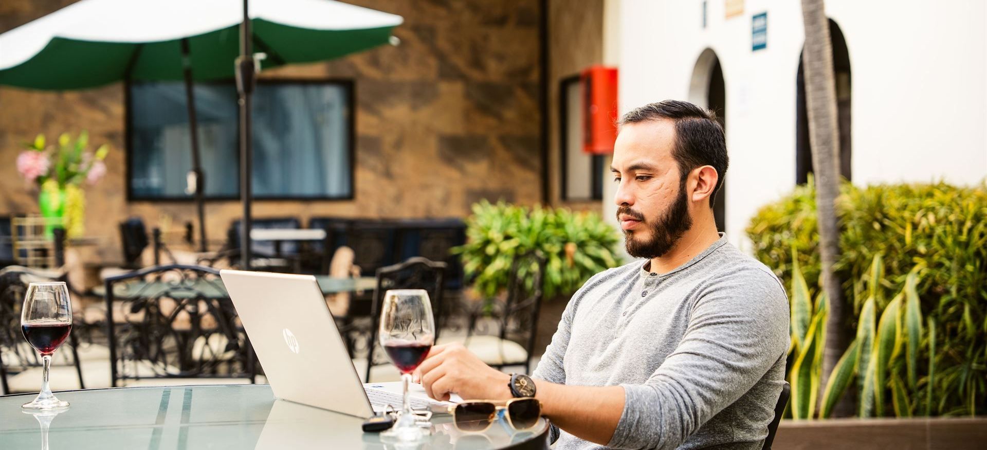 Un hombre está sentado en una mesa con una computadora portátil y una copa de vino.