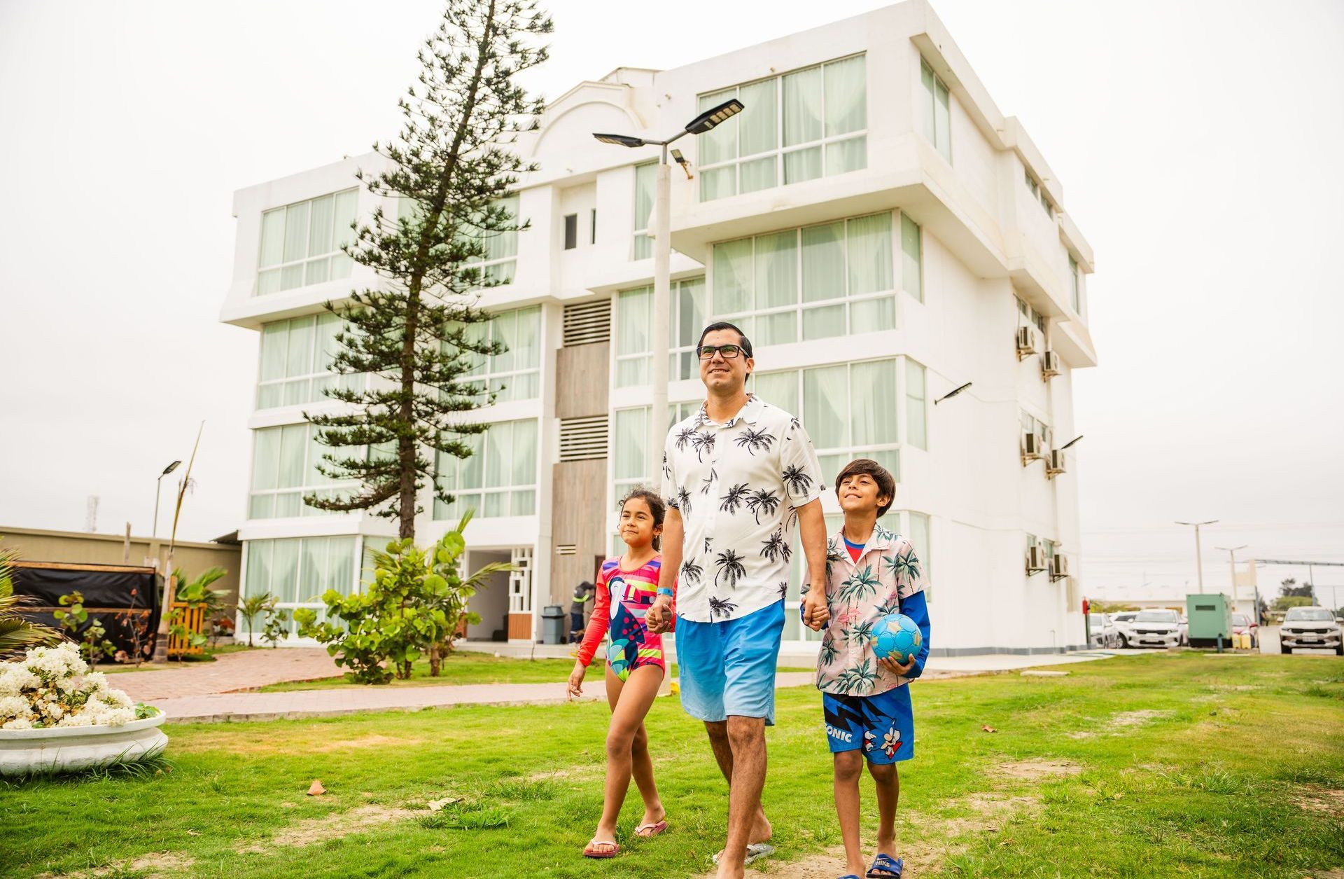 Un hombre y dos niños caminan frente a un edificio blanco.