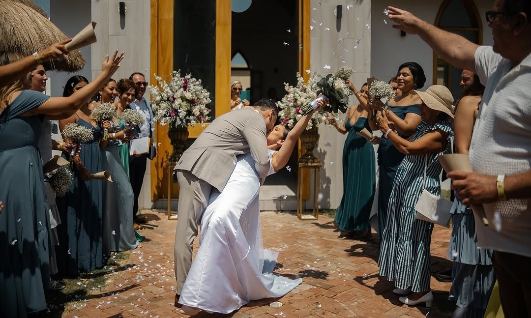 Una novia y un novio se besan frente a su fiesta nupcial.