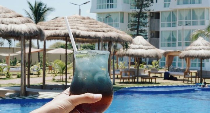 Una persona sostiene una bebida frente a una piscina.