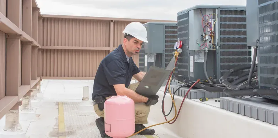 A man is working on an air conditioner on the roof of a building.