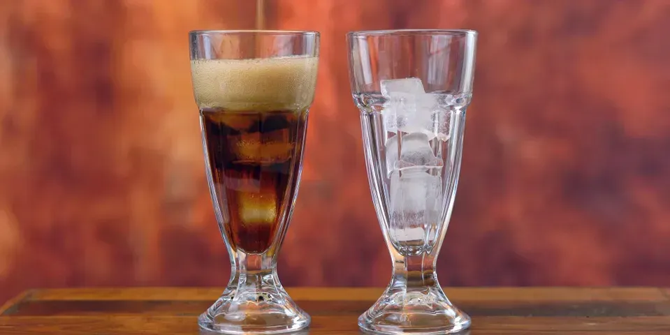 Two glasses of beer and ice are sitting on a wooden table.
