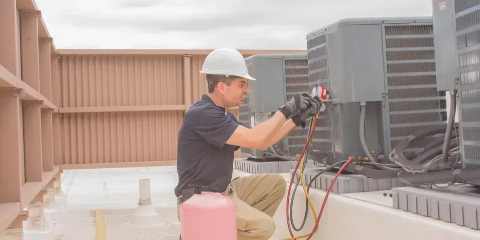 A man is working on an air conditioner on the roof of a building.