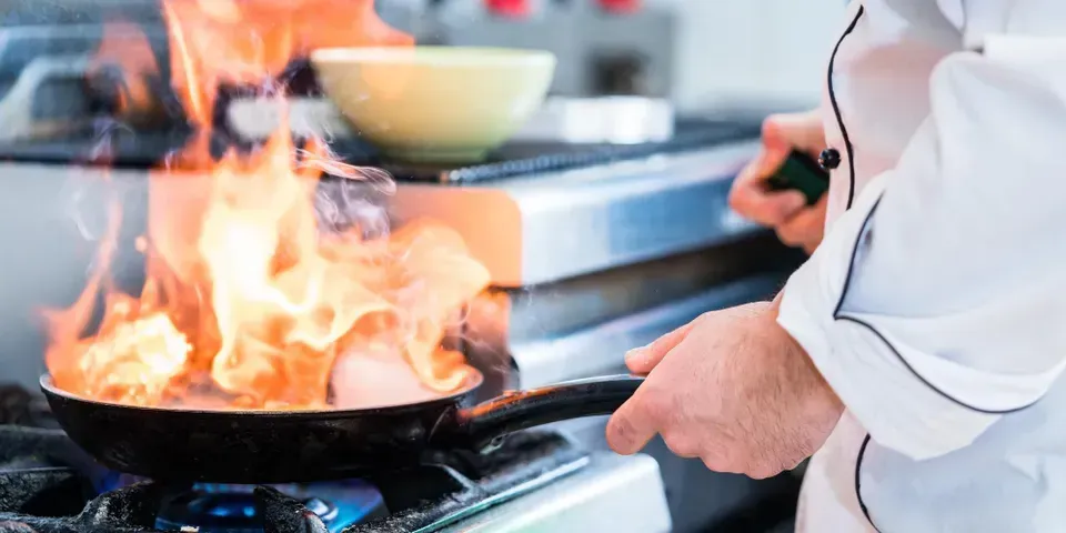 A chef is cooking food in a frying pan on a stove.