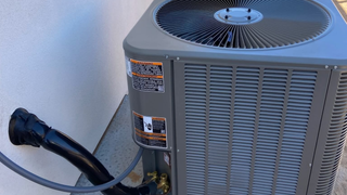 Outdoor air conditioning unit beside a wall, with black power cable and gray vents.