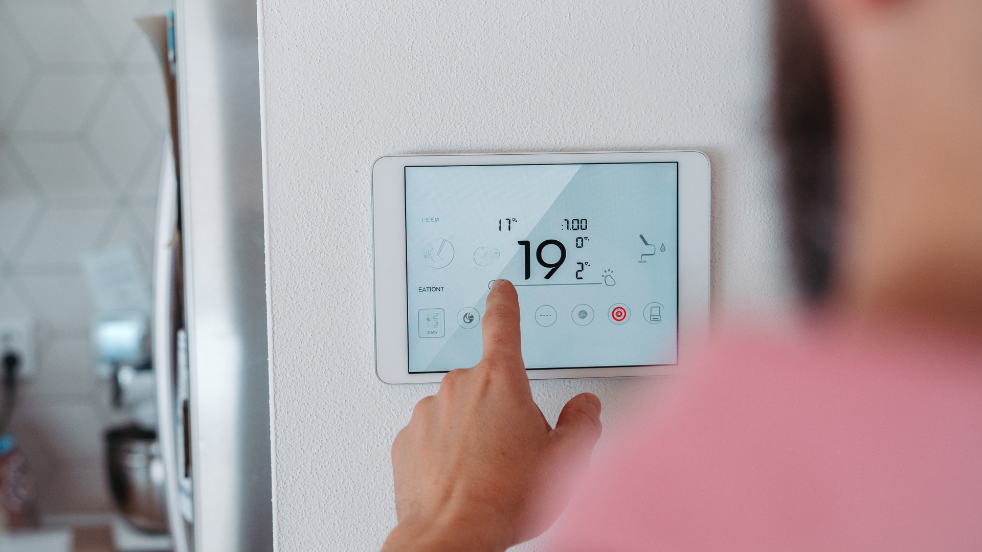 Hand adjusting a white wall thermostat showing 19° in a home interior