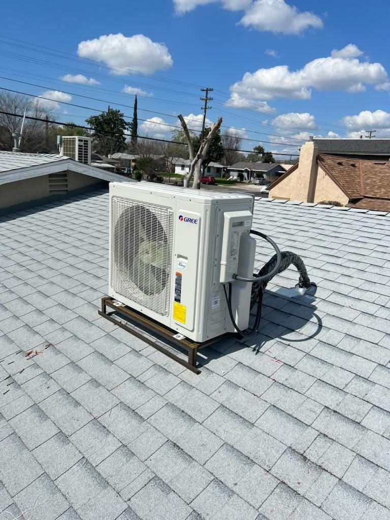 Rooftop HVAC unit on a gray shingle roof under a blue sky with clouds.