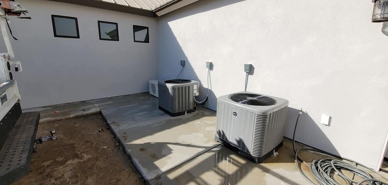 Outdoor rooftop patio with two air-conditioning units, white walls, and a small patch of dirt and concrete flooring