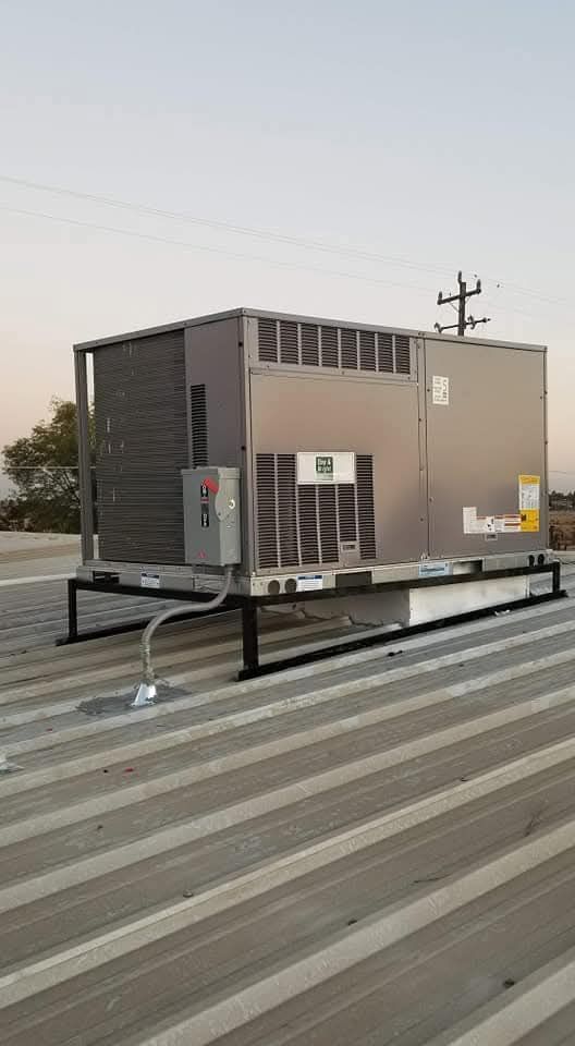 Rooftop HVAC unit on a metal platform above a corrugated roof at dusk.