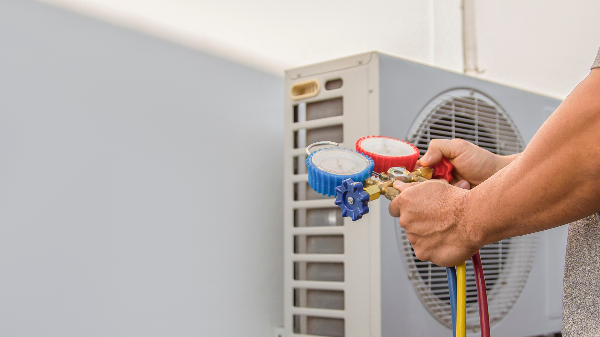 Technician connecting gauges to an outdoor air conditioner unit for maintenance