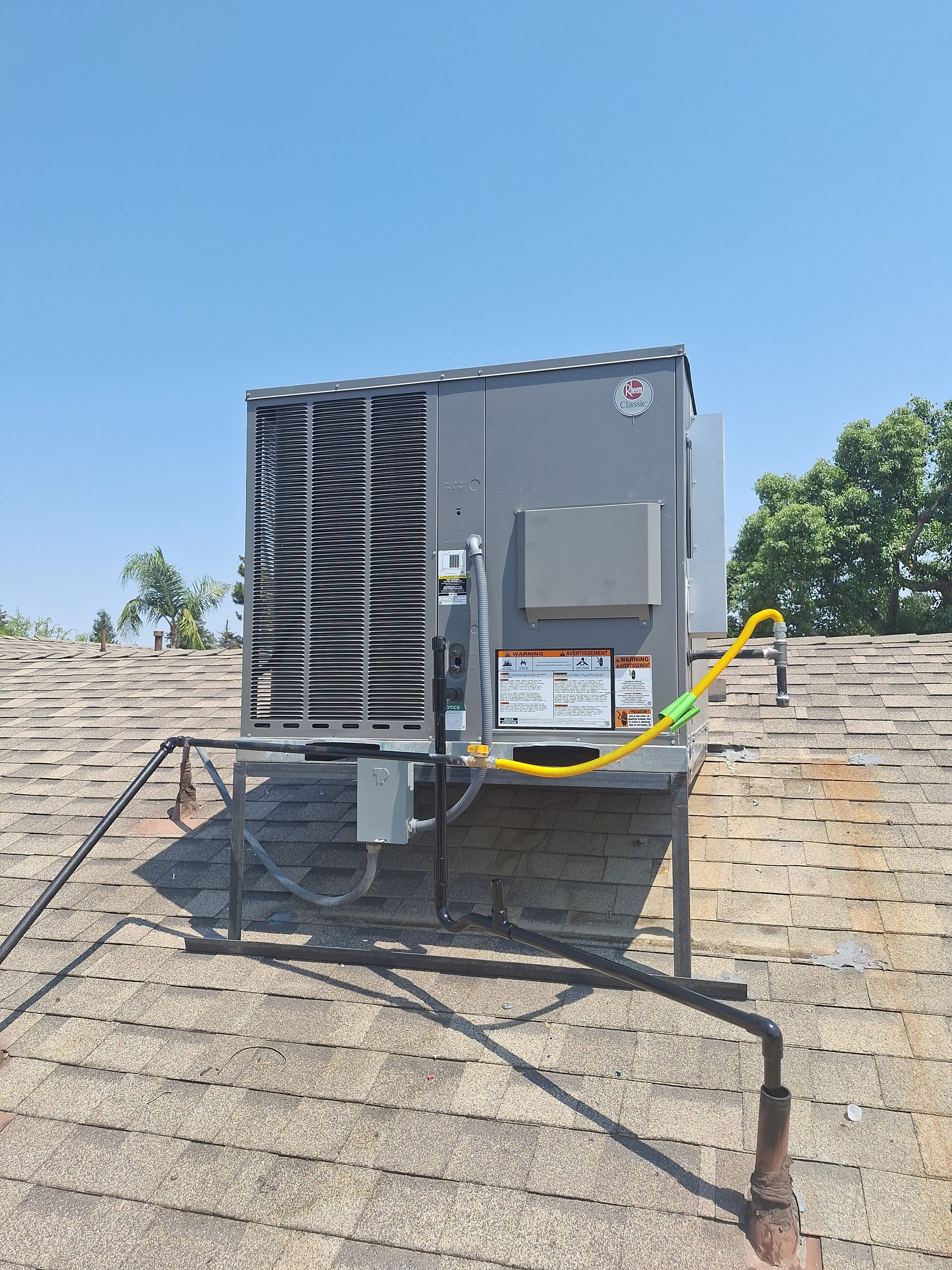 Roof-mounted HVAC unit on a shingled roof under a clear blue sky