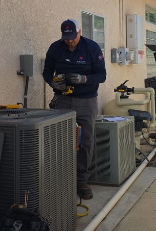 Technician in red overalls testing an electrical panel on a white wall with a ladder nearby