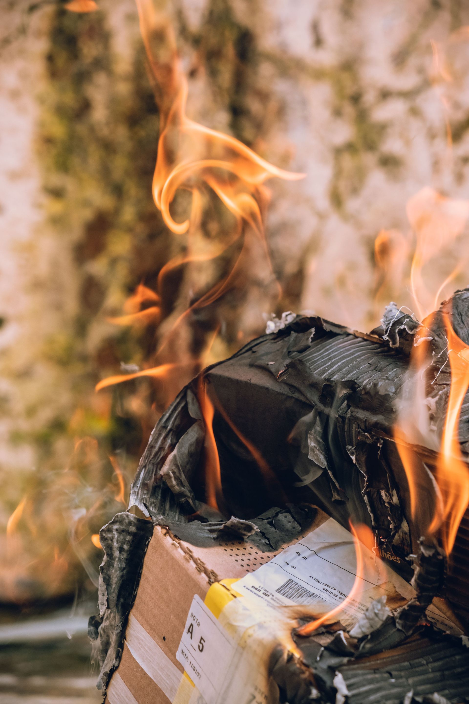 Burning trash pile with flames rising from a charred cardboard box outdoors