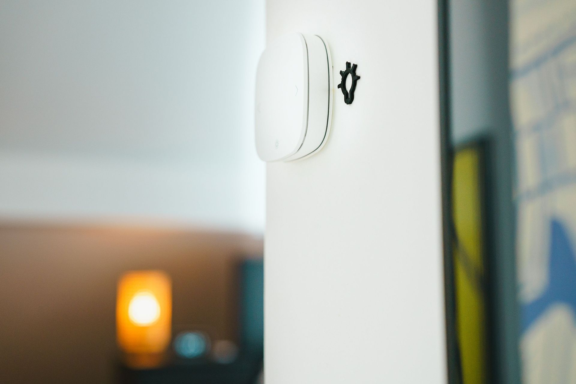 White wall-mounted device on a white pillar, with a blurred warm light in the background.