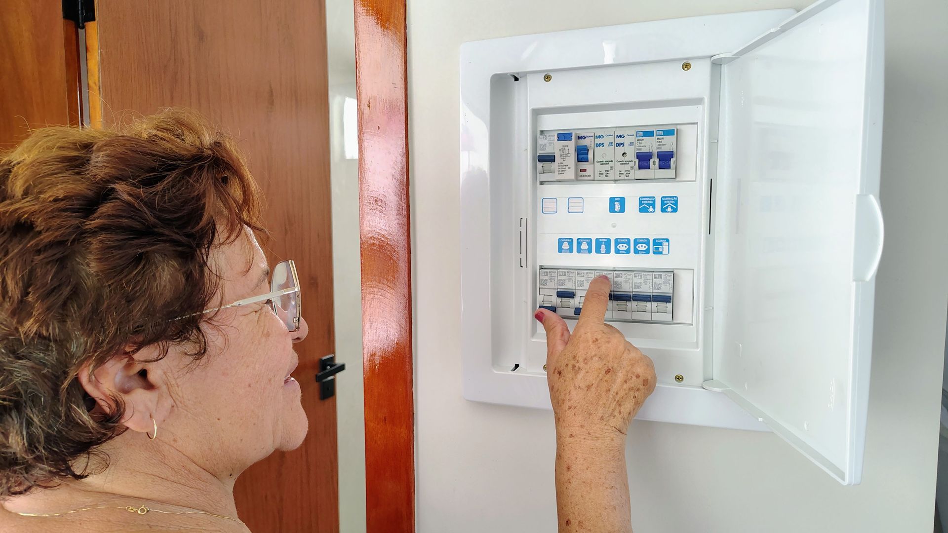 Person opening a white electrical breaker panel indoors with a hand on the switches