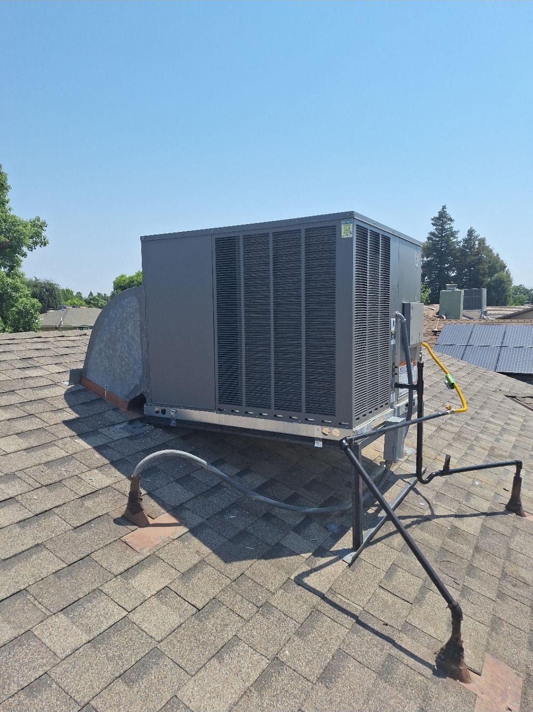 Roof-mounted HVAC unit on shingled rooftop with connected cables and ducting.
