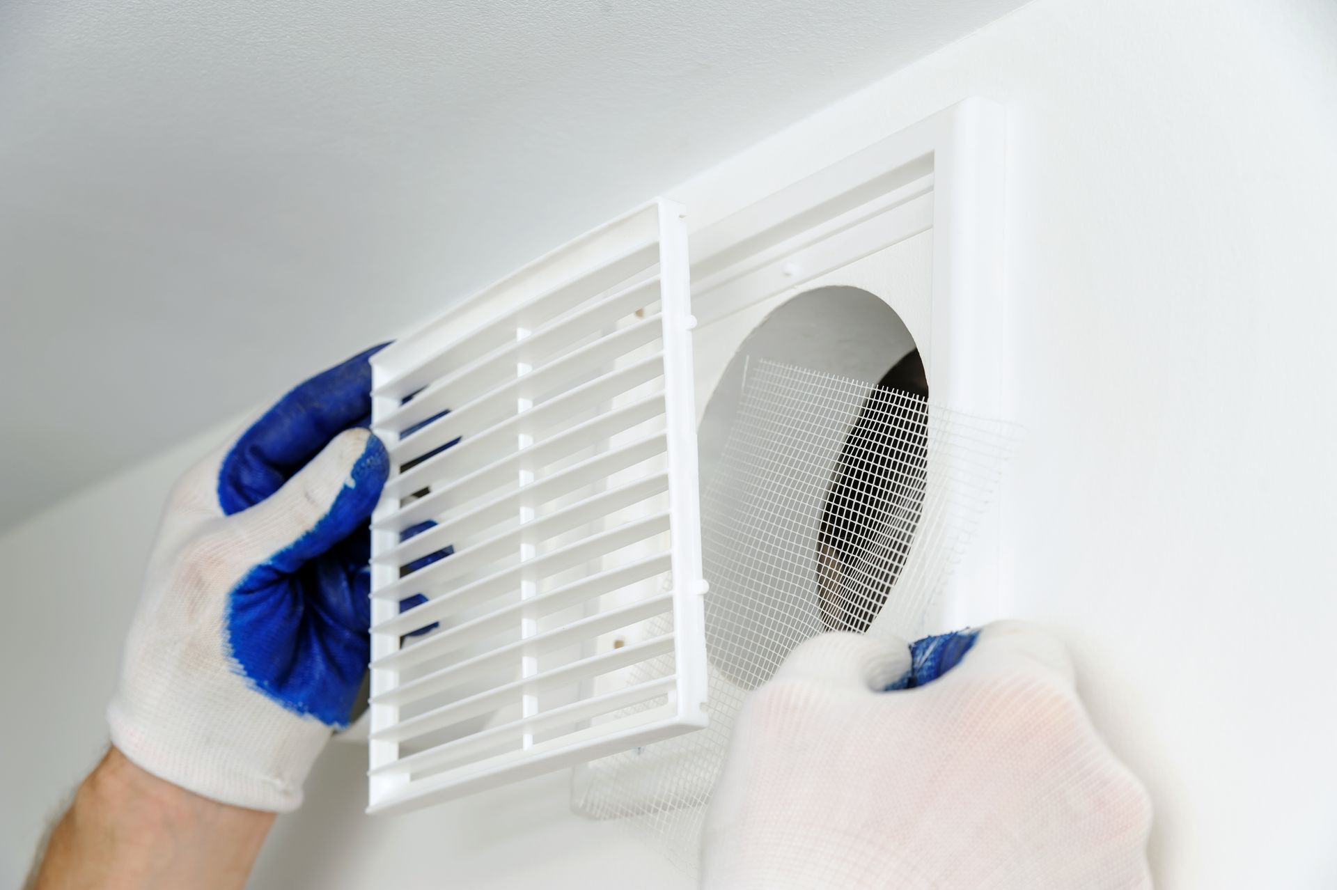 Gloved hands remove a vent cover beside a wall air filter.