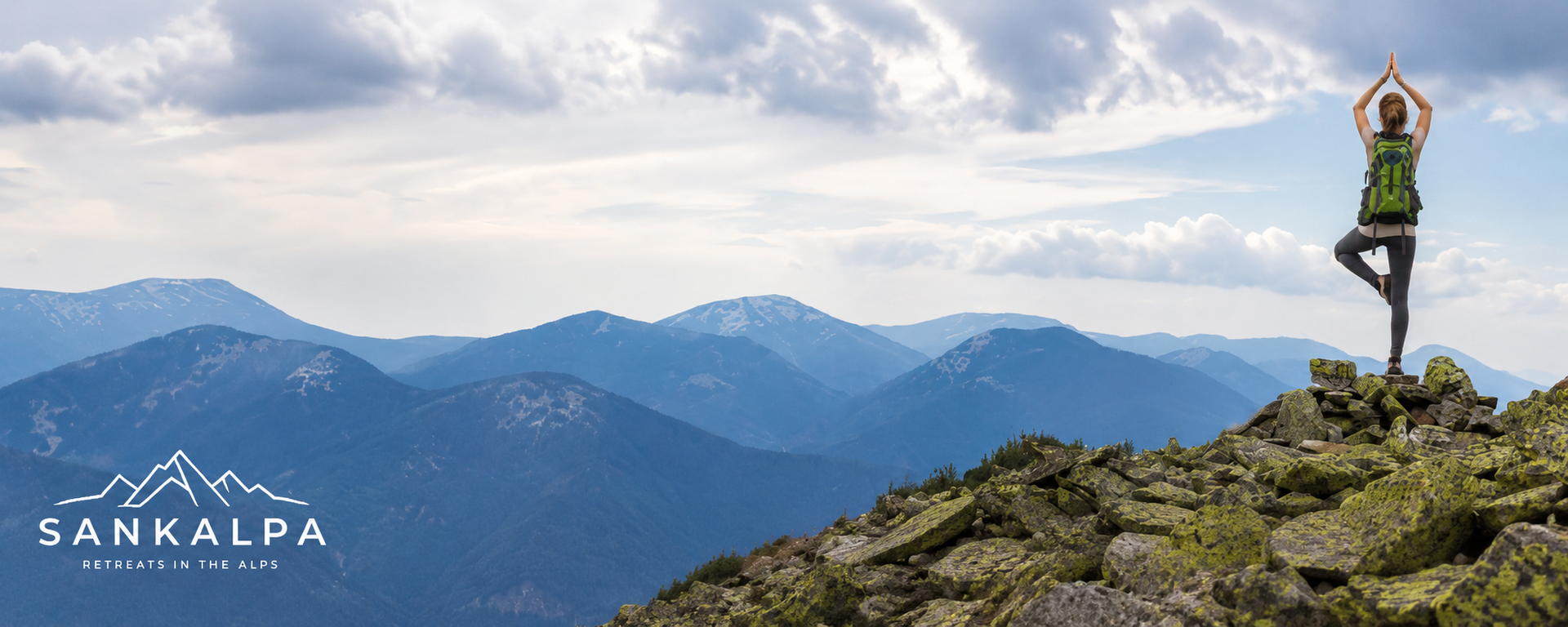 Person doing yoga on rocky mountain peak at sunrise, with blue mountain range and Sankalpa logo.