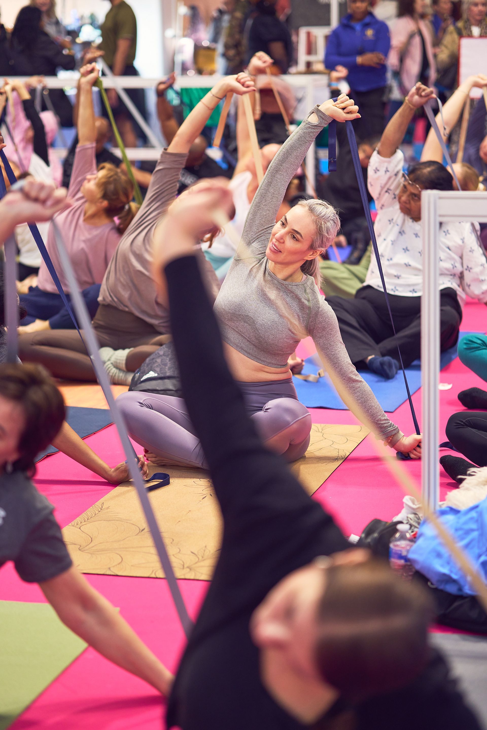 People in a fitness class stretching on colorful mats with raised arms and straps