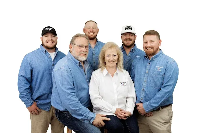 Group of six smiling coworkers in blue shirts and one white shirt posing against a white background