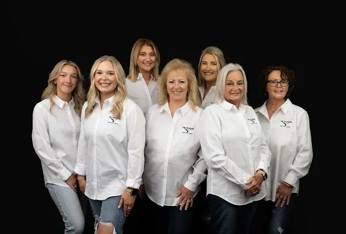 Six people in white shirts posing together against a black background.