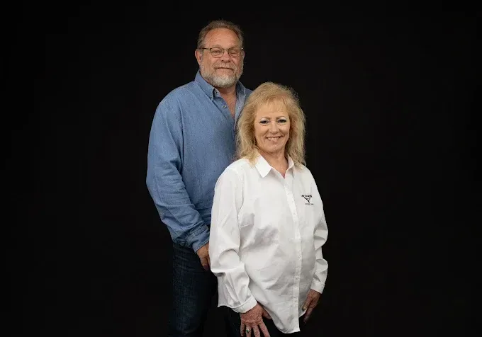 Two people posing against a black background, one in a white shirt and one in a blue shirt.