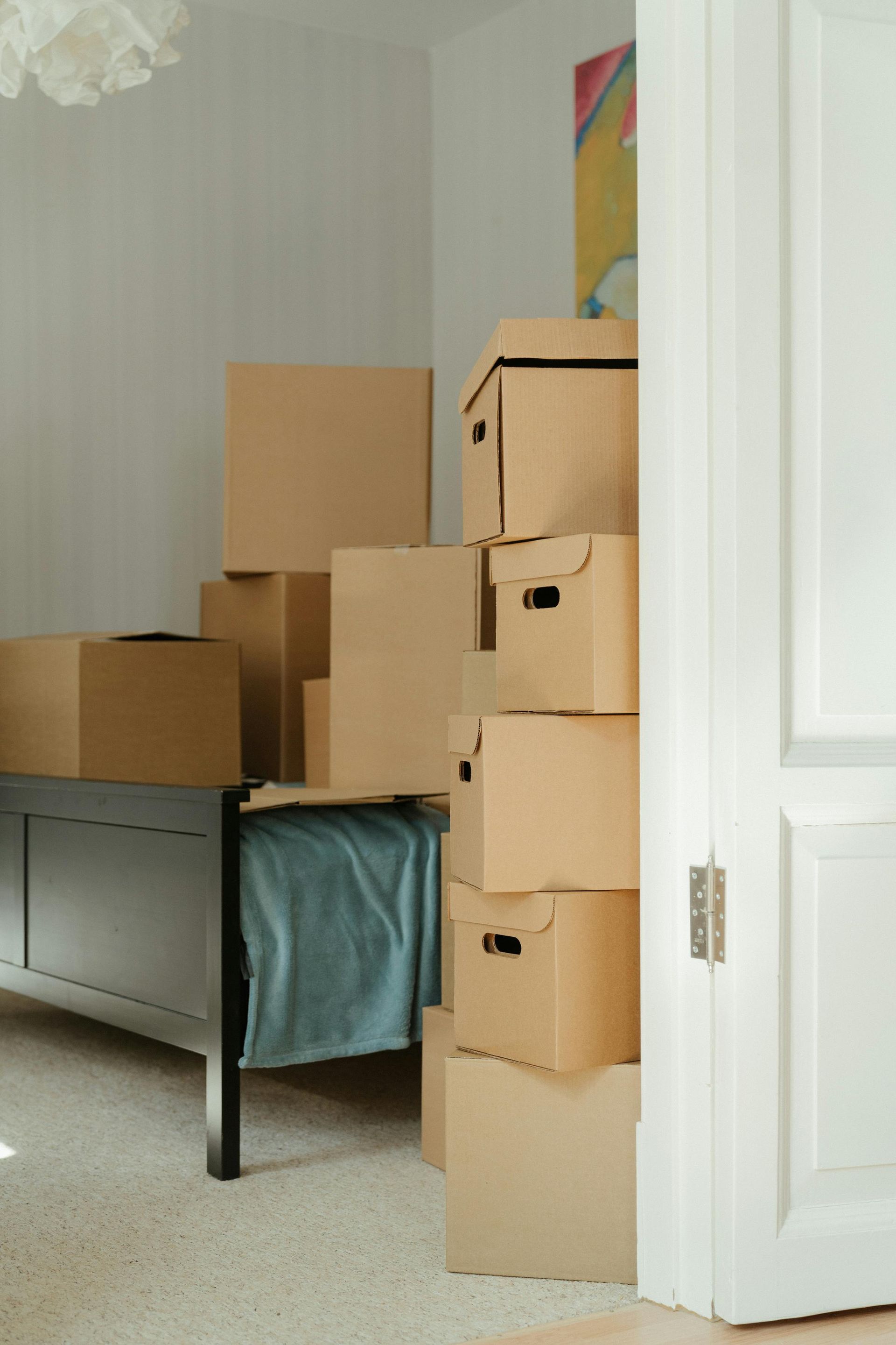 Stacked moving boxes in a bedroom beside a bed and open door