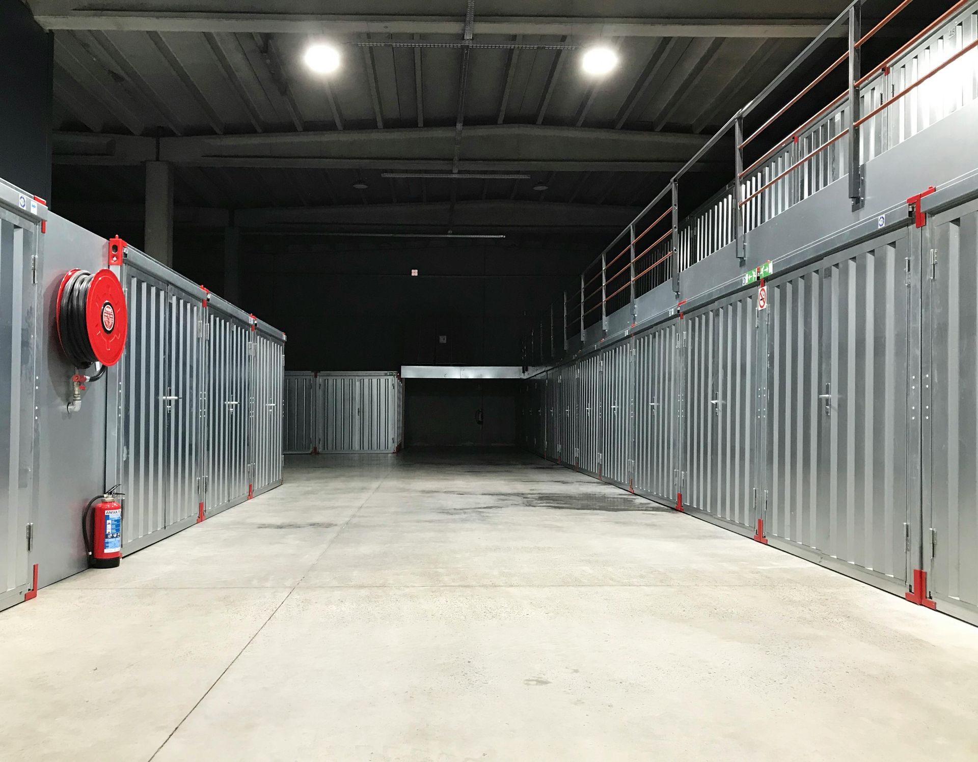 Empty storage unit hallway with gray doors, red fire equipment, and overhead lights