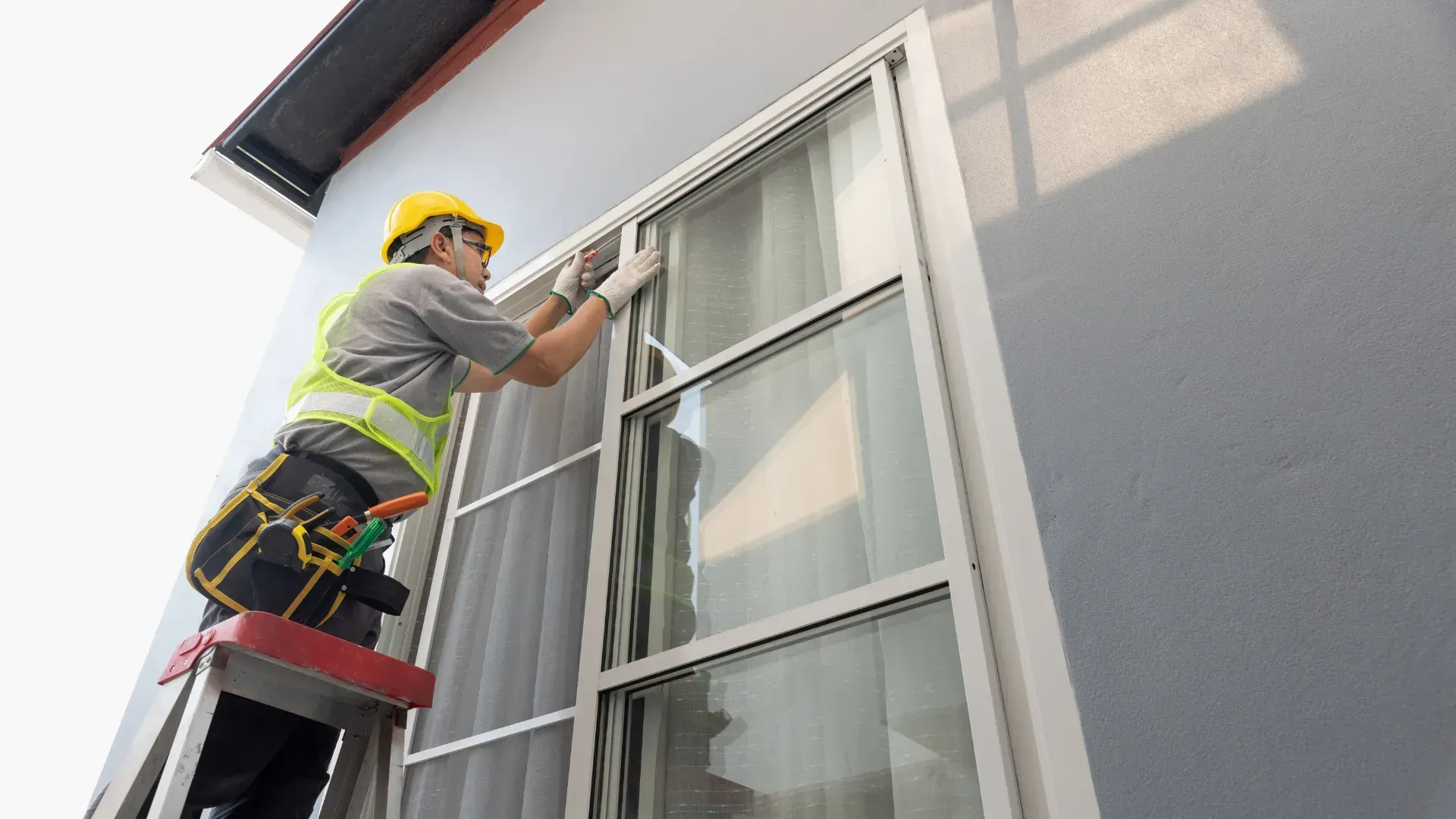 A man is standing on a ladder fixing a window.