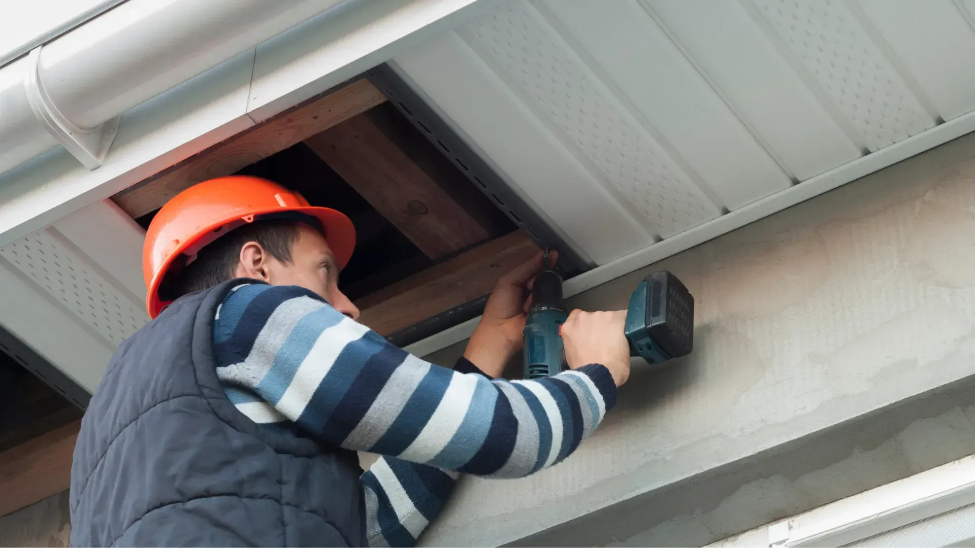 A man wearing a hard hat is working on a ceiling with a drill.