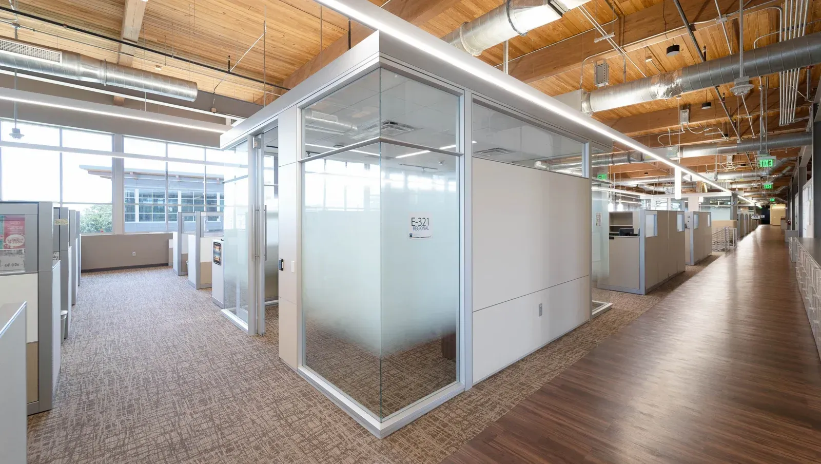 Modern office interior with glass-walled meeting rooms and open workspace under exposed wooden ceilings