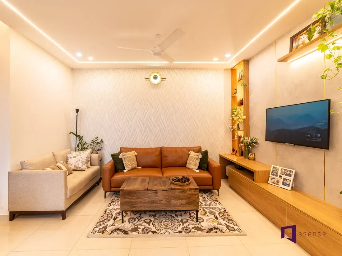 Modern living room with beige sofa, brown armchair, wooden coffee table, wall TV, and warm ceiling lights