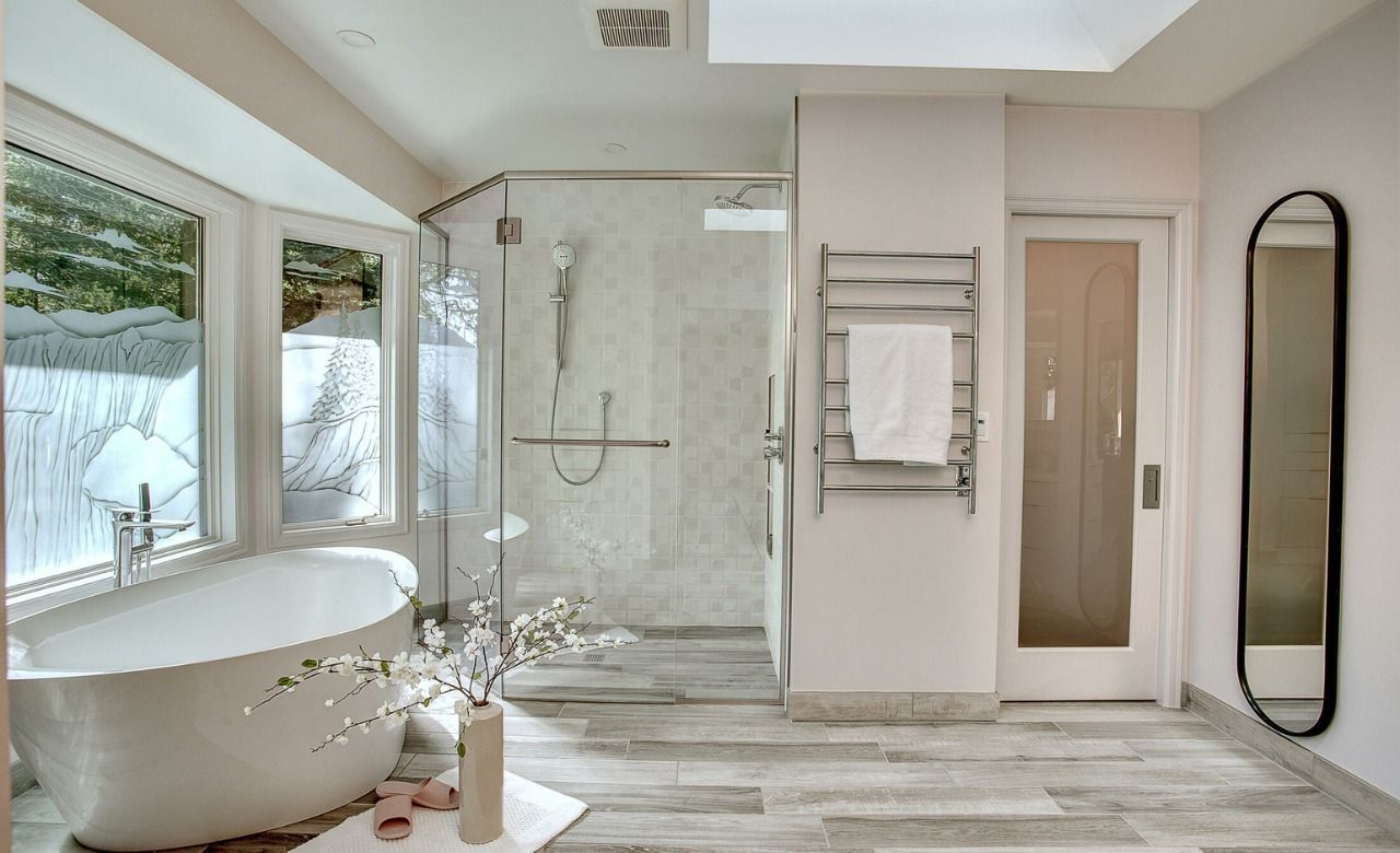 Bright modern bathroom with freestanding tub, glass shower, double windows, and light wood flooring