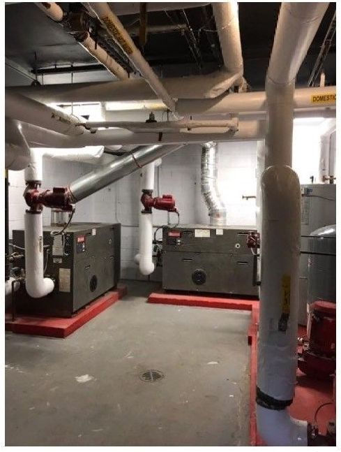 Industrial basement with boilers, red piping, and insulated ductwork in a utility room