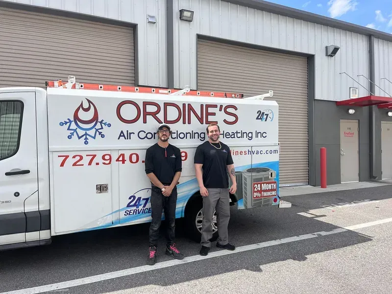 Two workers standing in front of an Ordine’s Air Conditioning & Heating service van outside a building
