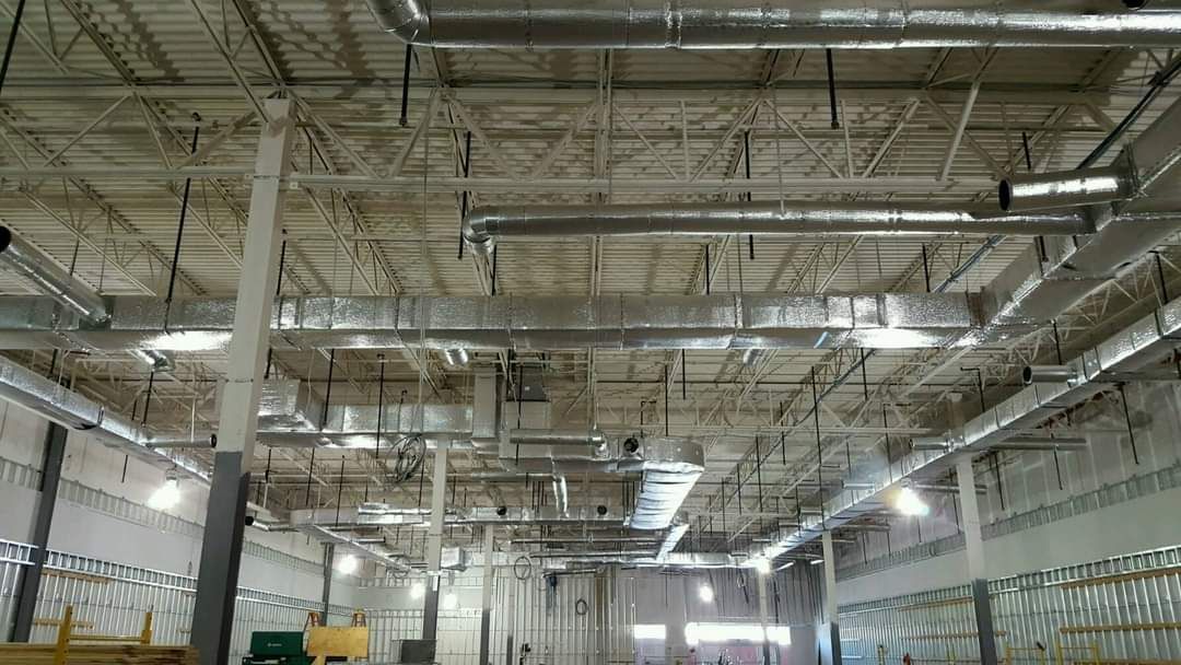 Industrial warehouse ceiling with exposed beams, pipes, and bright overhead lights