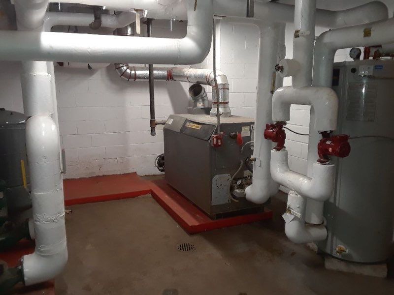 Industrial basement with white pipes, a gray boiler unit, and a green tank on a concrete floor.
