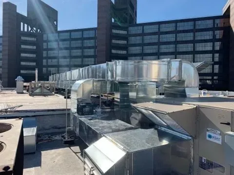 Rooftop HVAC ductwork and metal vents on a building roof with city office buildings in the background