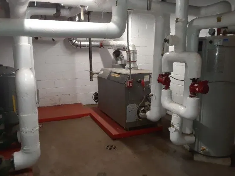 Industrial boiler room with white pipes and gray machinery on a red floor.