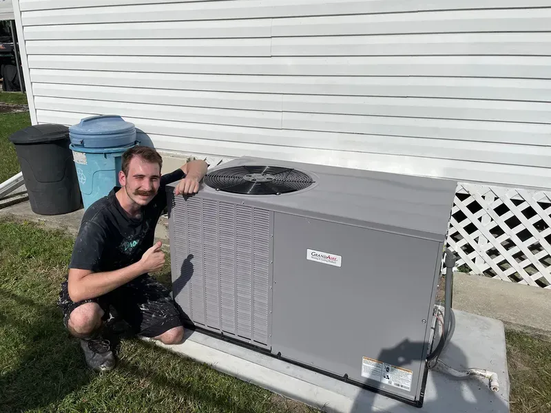 Man crouching beside a gray outdoor air conditioner unit next to a house wall