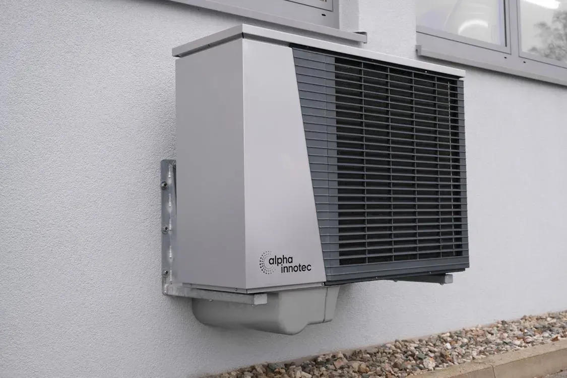 Wall-mounted outdoor HVAC unit with black vented front on a gray building wall.