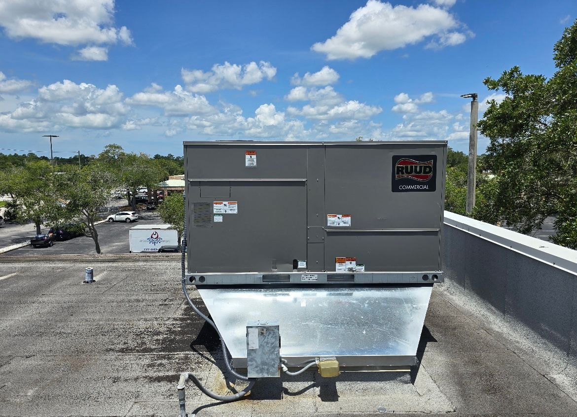 Rooftop HVAC unit with metal ducting under a bright blue sky and clouds.