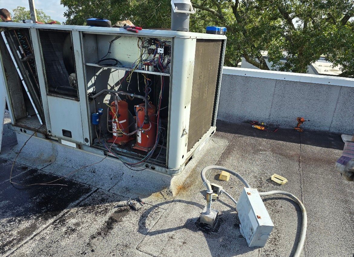 Open rooftop HVAC unit with exposed wiring and tools on gravel surface